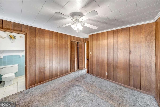 carpeted empty room featuring ceiling fan, wooden walls, and ornamental molding