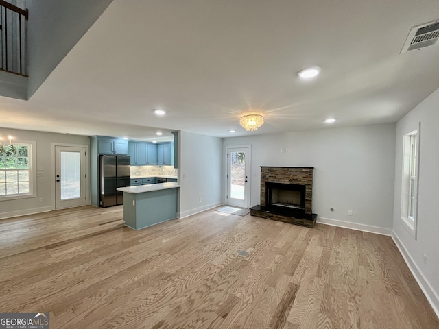 unfurnished living room featuring light hardwood / wood-style flooring, an inviting chandelier, and a stone fireplace