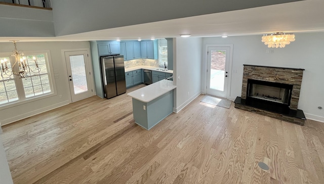 kitchen featuring light hardwood / wood-style flooring, a notable chandelier, backsplash, a fireplace, and appliances with stainless steel finishes