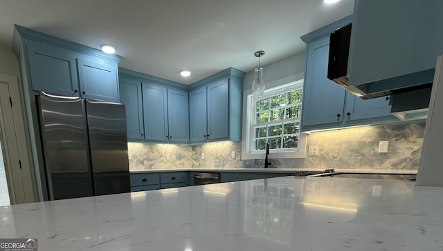 kitchen featuring stainless steel fridge, tasteful backsplash, light stone counters, sink, and decorative light fixtures