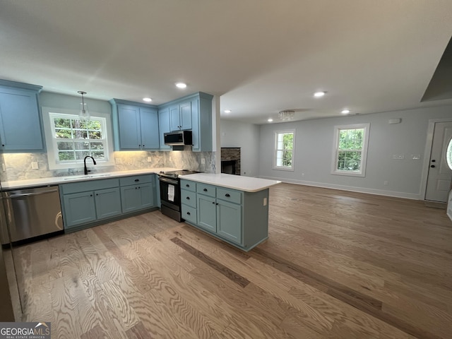 kitchen with kitchen peninsula, stainless steel appliances, sink, decorative light fixtures, and light hardwood / wood-style floors