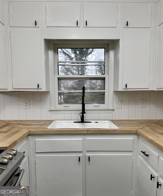 kitchen with butcher block counters, white cabinets, a sink, and stainless steel gas range oven