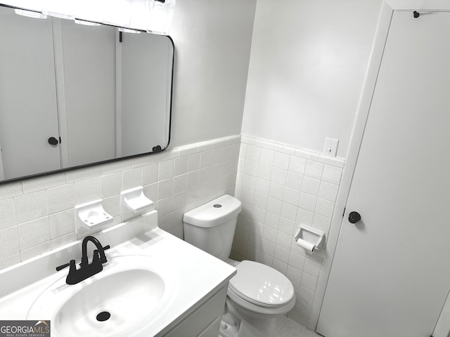 half bathroom featuring wainscoting, vanity, toilet, and tile walls