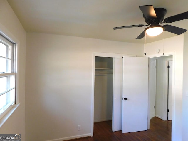 unfurnished bedroom featuring dark wood-style floors, a closet, baseboards, and a ceiling fan