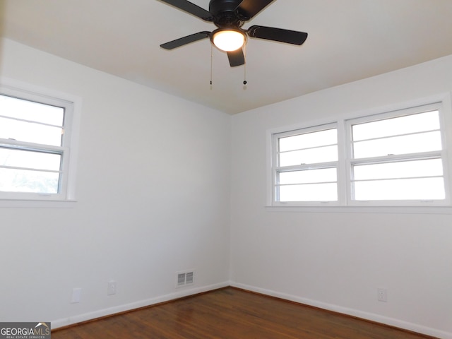 unfurnished room featuring a healthy amount of sunlight, baseboards, visible vents, and dark wood-style flooring