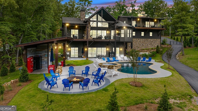 back house at dusk with a yard, a balcony, a patio, and an outdoor fire pit