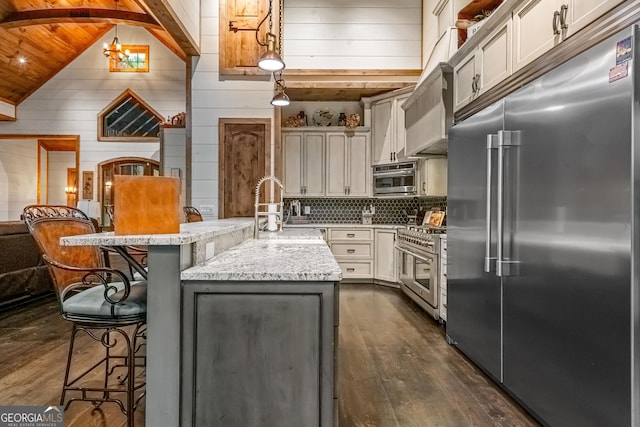 kitchen featuring hanging light fixtures, light stone counters, high quality appliances, a kitchen island with sink, and a breakfast bar