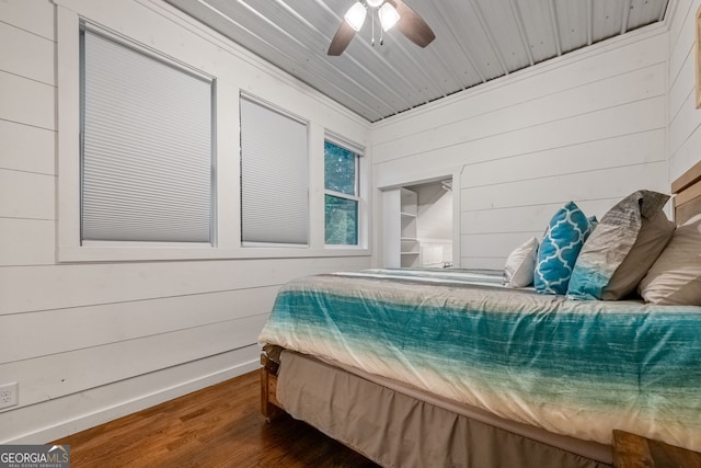 bedroom with ceiling fan, wood ceiling, dark wood-type flooring, and wooden walls