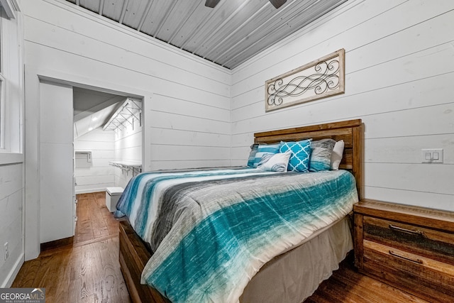 bedroom with hardwood / wood-style floors, connected bathroom, ceiling fan, and wood walls