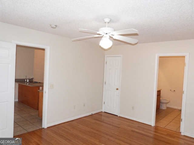 unfurnished bedroom featuring sink, ensuite bath, light hardwood / wood-style flooring, and a textured ceiling