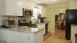 kitchen featuring kitchen peninsula, white cabinetry, black appliances, and light stone counters