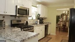 kitchen featuring white cabinetry, sink, light stone counters, black appliances, and hardwood / wood-style flooring