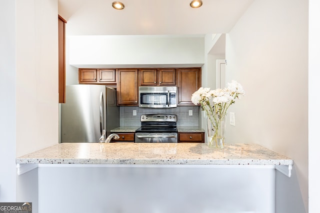 kitchen featuring light stone countertops, appliances with stainless steel finishes, backsplash, and kitchen peninsula