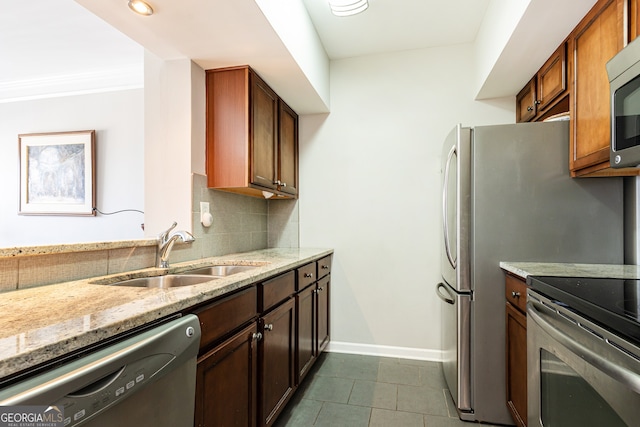 kitchen featuring light stone countertops, appliances with stainless steel finishes, tasteful backsplash, dark tile patterned floors, and sink