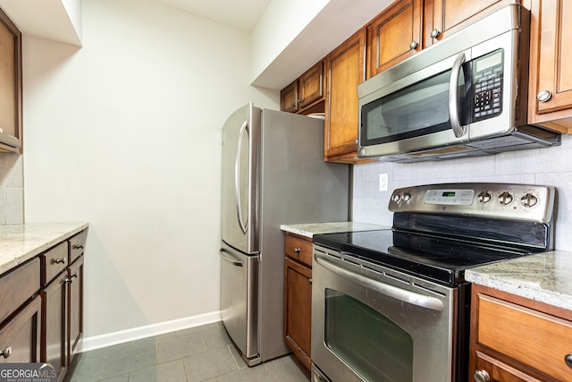 kitchen featuring dark tile patterned floors, light stone countertops, and appliances with stainless steel finishes