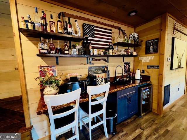 bar featuring hardwood / wood-style flooring, wine cooler, blue cabinets, and wooden walls