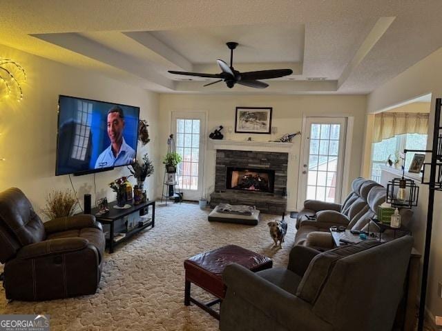 living room featuring carpet flooring, ceiling fan, a fireplace, and a tray ceiling