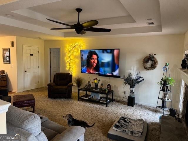 carpeted living room with ceiling fan and a tray ceiling