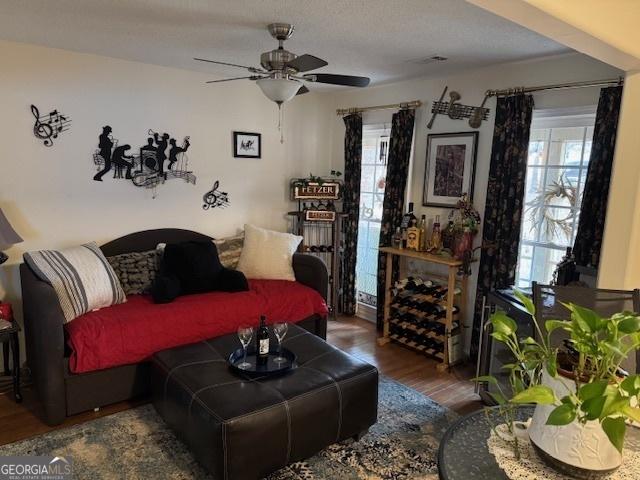 living room featuring ceiling fan, dark wood-type flooring, and a textured ceiling