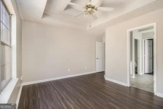 spare room with a raised ceiling, ceiling fan, and dark wood-type flooring