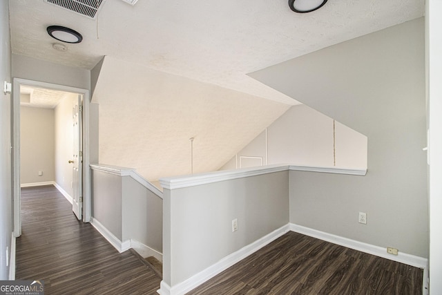 hallway with dark hardwood / wood-style floors, a textured ceiling, and vaulted ceiling