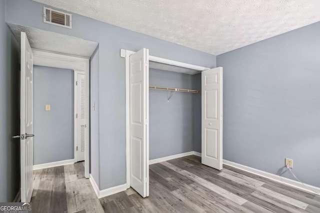 unfurnished bedroom with wood-type flooring, a textured ceiling, and a closet