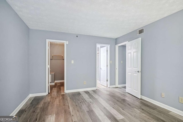 unfurnished bedroom with a spacious closet, a closet, a textured ceiling, and light wood-type flooring