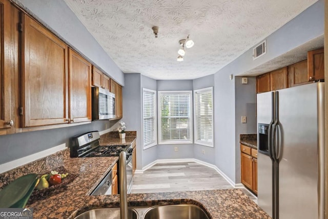 kitchen featuring appliances with stainless steel finishes, a textured ceiling, light hardwood / wood-style flooring, and dark stone countertops