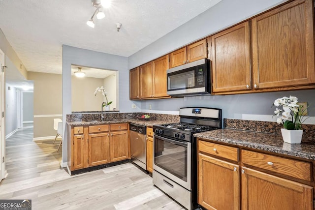 kitchen with sink, stainless steel appliances, dark stone counters, a textured ceiling, and light wood-type flooring