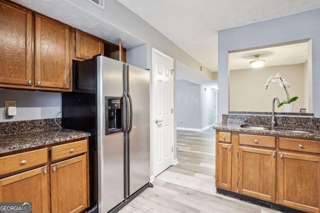 kitchen featuring stainless steel fridge, light hardwood / wood-style flooring, dark stone counters, and sink