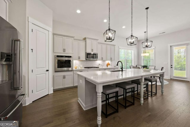 kitchen featuring appliances with stainless steel finishes, light stone counters, sink, white cabinets, and hanging light fixtures