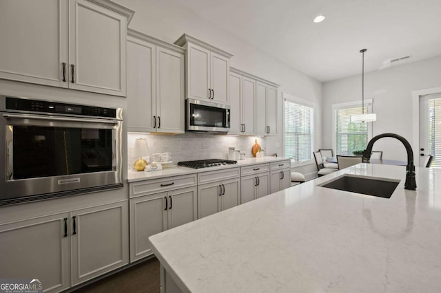 kitchen with white cabinetry, sink, pendant lighting, a kitchen island with sink, and appliances with stainless steel finishes