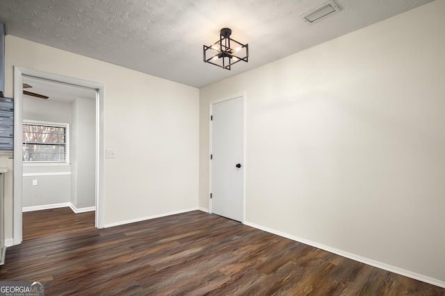 empty room with a textured ceiling, dark hardwood / wood-style floors, and an inviting chandelier