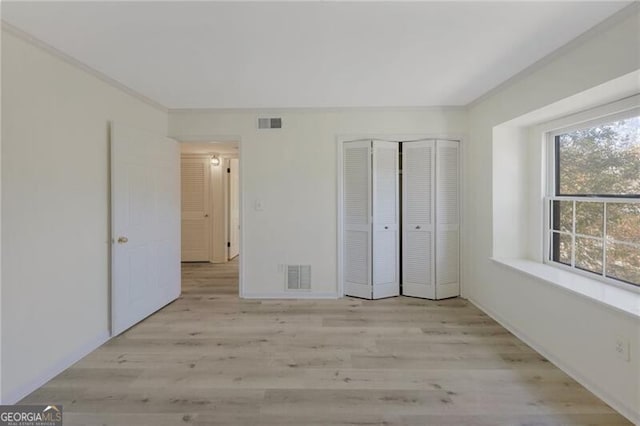 unfurnished bedroom featuring light hardwood / wood-style floors, ornamental molding, and a closet