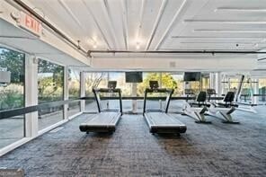 gym with a wall of windows and dark colored carpet