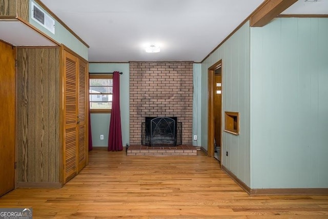 unfurnished living room with a fireplace, light hardwood / wood-style flooring, crown molding, and wood walls