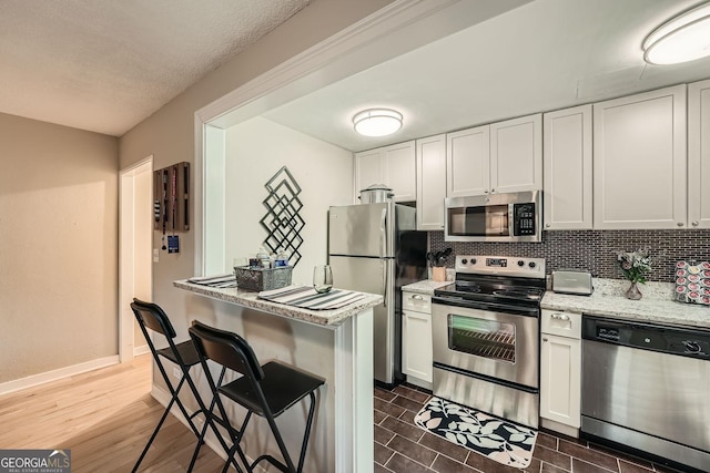 kitchen with light stone countertops, backsplash, a breakfast bar, white cabinets, and appliances with stainless steel finishes