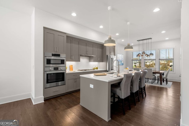 kitchen featuring stainless steel appliances, decorative light fixtures, dark hardwood / wood-style flooring, a kitchen island with sink, and gray cabinetry