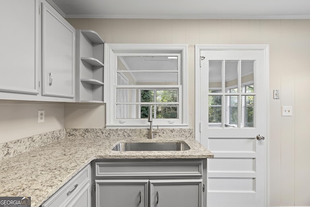 kitchen with white cabinetry, light stone counters, sink, and wooden walls