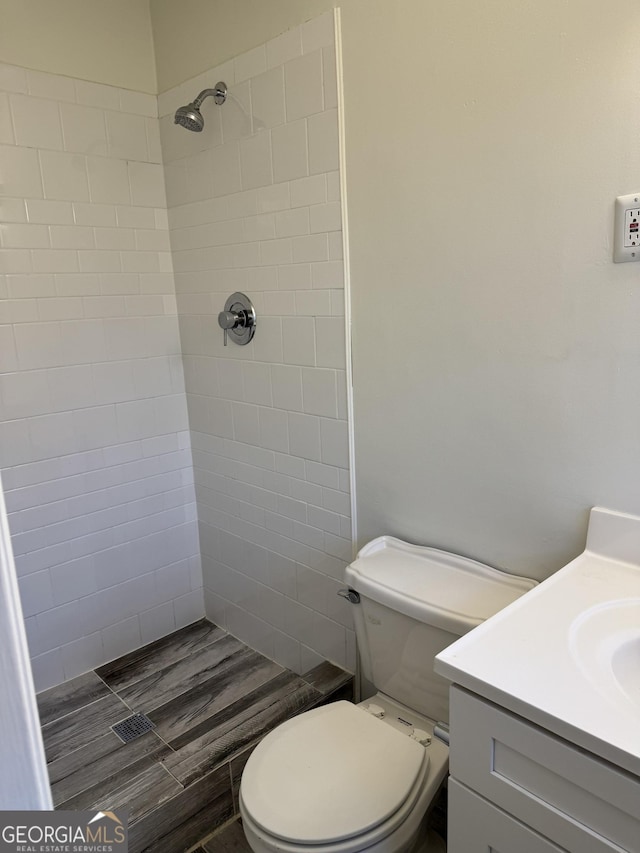 bathroom featuring a tile shower, vanity, and toilet