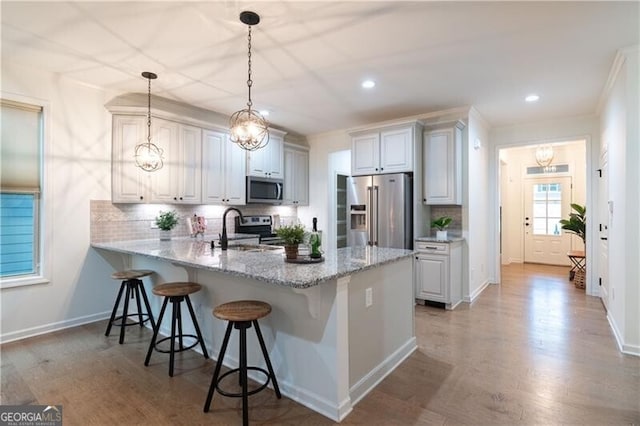 kitchen with kitchen peninsula, appliances with stainless steel finishes, backsplash, decorative light fixtures, and white cabinetry