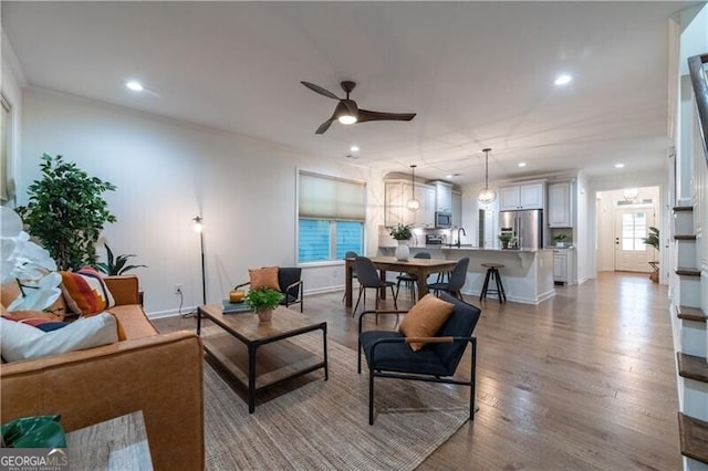 living room featuring ceiling fan, light wood-type flooring, and crown molding