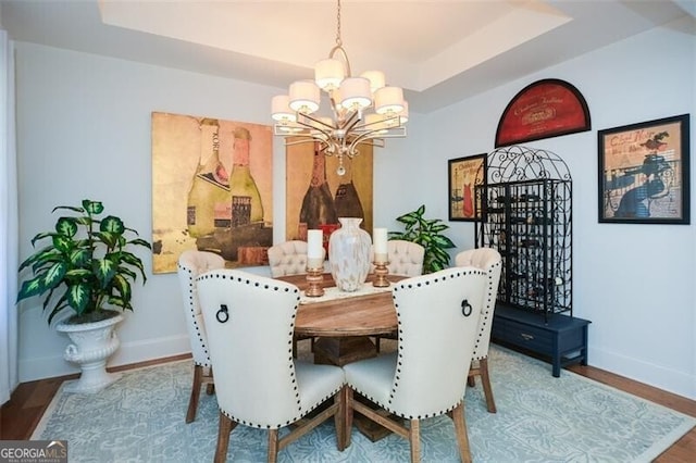 dining room with hardwood / wood-style floors, an inviting chandelier, and a raised ceiling