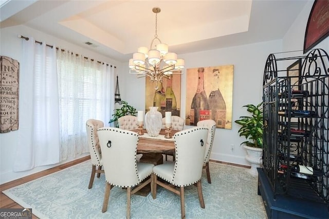 dining area with hardwood / wood-style floors, a raised ceiling, and a notable chandelier