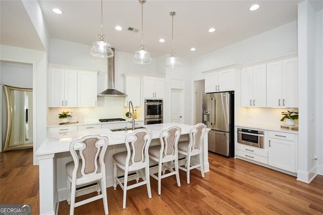 kitchen with white cabinets, hanging light fixtures, wall chimney exhaust hood, tasteful backsplash, and stainless steel appliances