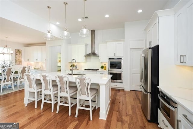 kitchen with appliances with stainless steel finishes, white cabinetry, and wall chimney exhaust hood