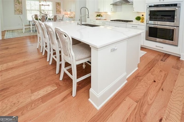 kitchen featuring white cabinets, sink, light wood-type flooring, an island with sink, and stainless steel appliances