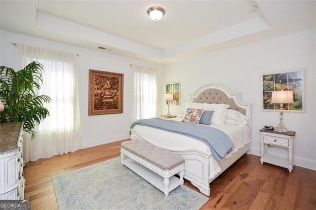 bedroom featuring multiple windows, a tray ceiling, and dark hardwood / wood-style floors