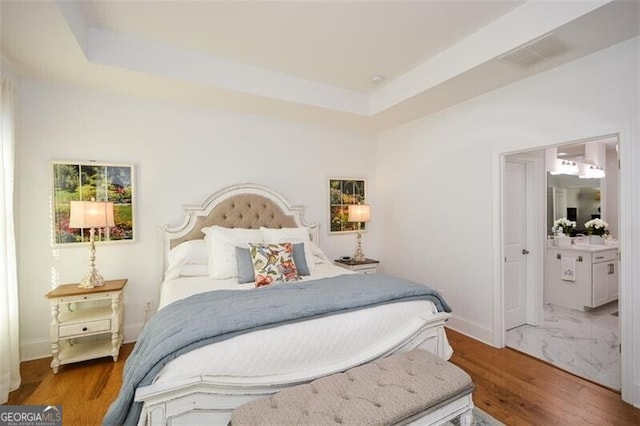 bedroom with a tray ceiling, ensuite bathroom, and hardwood / wood-style flooring