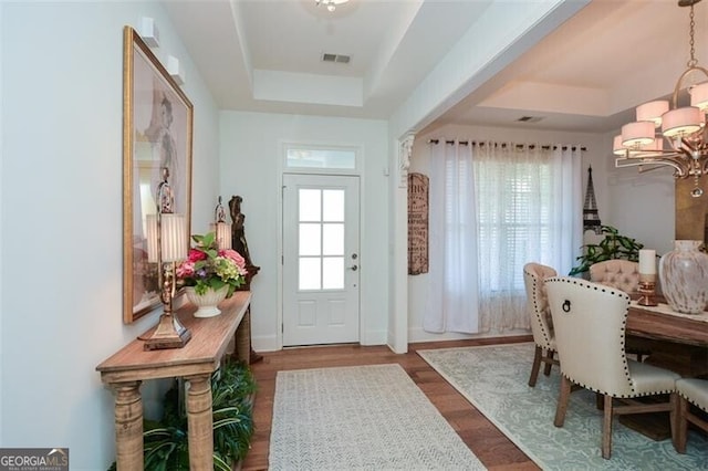 doorway to outside featuring a tray ceiling, dark hardwood / wood-style floors, and an inviting chandelier